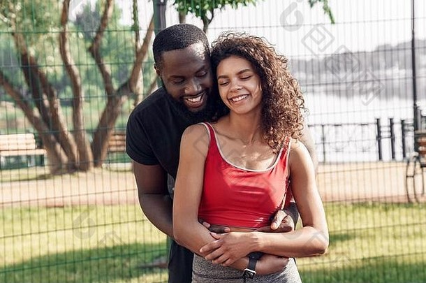 户外活动。一对非洲夫妇站在球场上微笑着拥抱