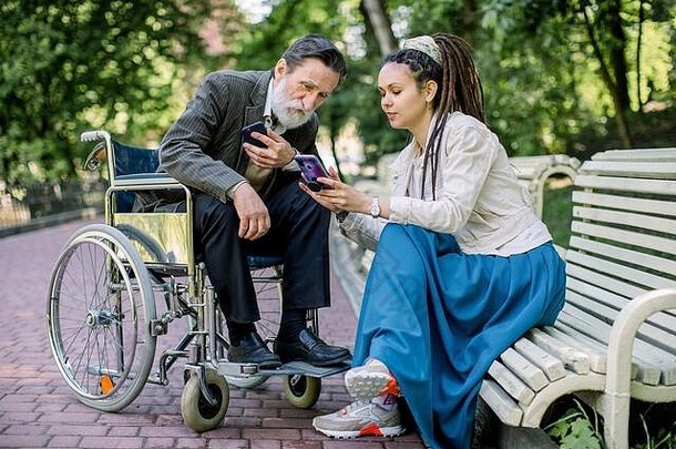 一位坐在轮椅上的老年患者，坐在公园的长椅上，与他的<strong>护理</strong>者、护士或孙女交谈，看着他们的眼睛