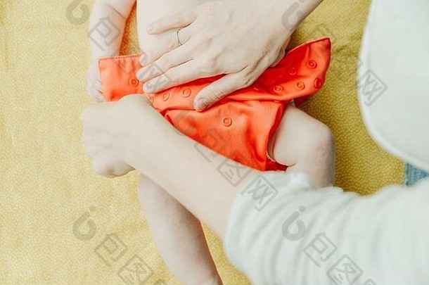 特写镜头是母亲给新生儿穿上橙色婴儿尿布的手。
