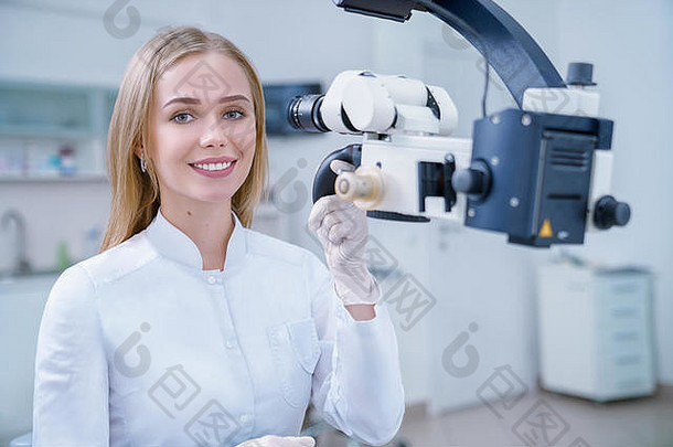 可爱的金发女郎女人工作口腔学家私人牙科诊所快乐的牙医相机微笑摆姿势专家工作现代设备牙科显微镜