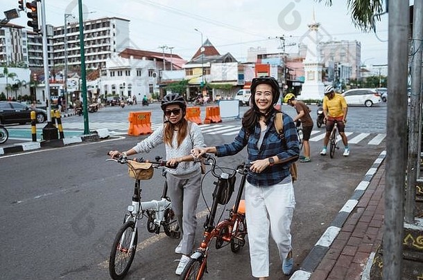 两名戴着头盔和包的亚洲年轻女子骑着折叠自行车行走