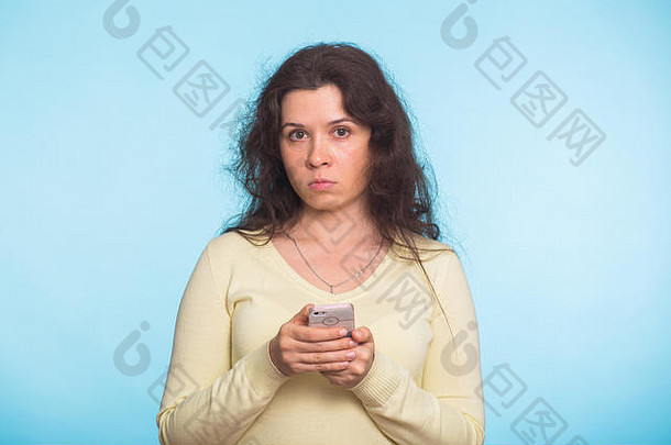 心怀不满的女人拿着智能手机看着蓝色背景上的摄像机