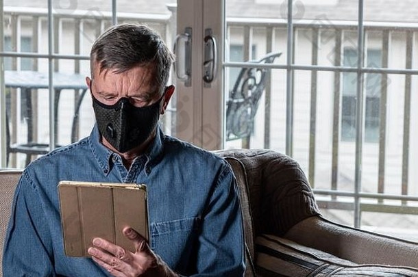 一名戴着防流感和冠状病毒防护口罩的忧心忡忡的男子正在平板电脑上阅读新闻