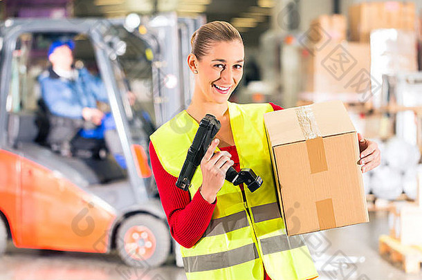 身穿防护背心和扫描仪的女工人手持包裹，微笑着站在货运公司的仓库前