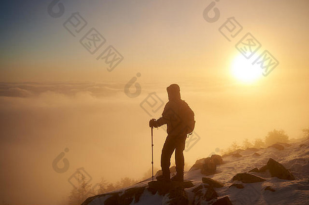 背着背包和登山杖的旅游徒步旅行者的后视图，他们休息在落基山脉的山顶上，背景是美丽的雾谷，在冬天的黎明时分，那里弥漫着白色的浮云。
