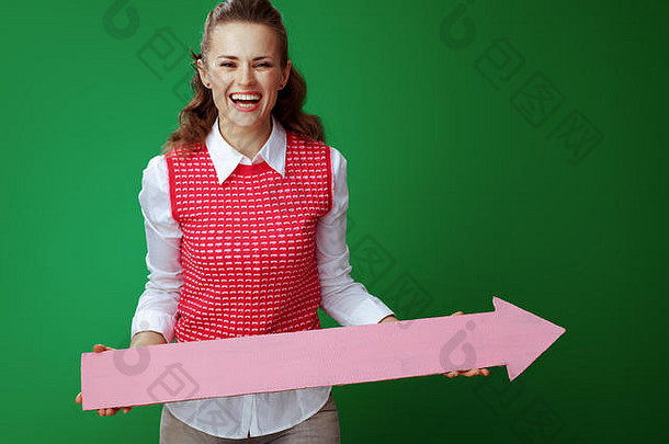 微笑年轻的学习者女人灰色牛仔裤粉红色的无袖衬衫持有大粉红色的箭头指出孤立的绿色