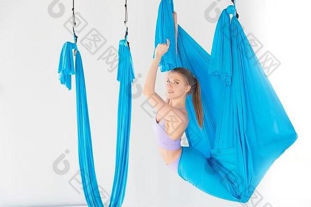 哈他航空飞行瑜伽概念。美丽的年轻女教练在白色工作室的蓝色吊床上展示伸展运动