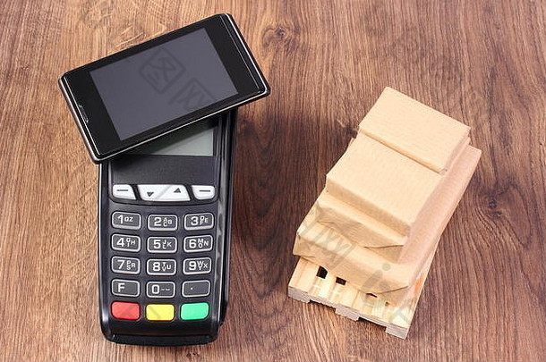 具有NFC技术的移动电话和木制托盘上的小包装盒的支付终端，用于支付产品和运输费用