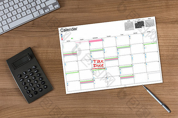 木制桌子上的日历，上面写着“税款到期”，配有计算器、现代键盘和银笔