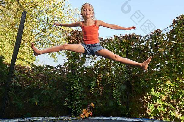可爱的金发女孩在绿色背景的蹦床上玩耍和跳跃