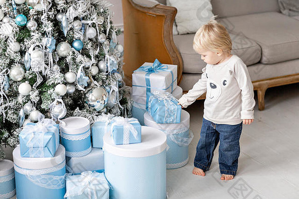 一个小男孩站在许多礼物旁边。新年快乐。装饰过的圣诞树。明亮的客厅里的圣诞节早晨
