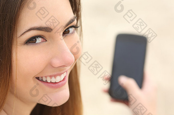 海滩上一个笑脸女人使用智能手机的特写照片