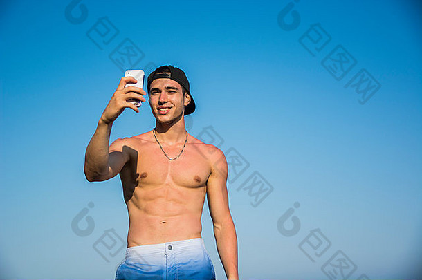 一边视图赤膊上阵年轻的男人。采取自拍照片海滩坐着大岩石热太阳