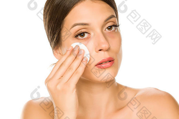 年轻漂亮的女人用白色背景的棉布擦脸