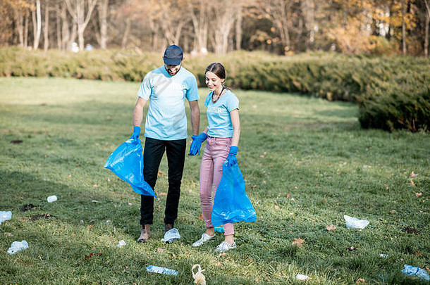 身穿蓝色t恤衫的男女志愿者正在清洁公共花园，将塑料垃圾放入袋子中