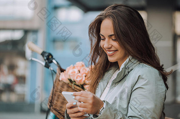 坐在城市的长椅上，快乐的年轻女子通过手机查看电子邮件