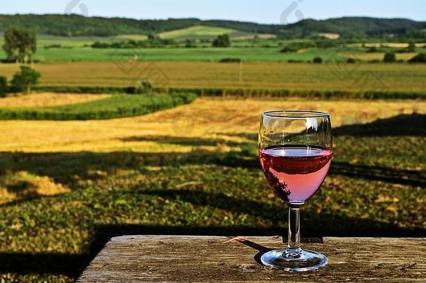 一杯有着美丽乡村背景的玫瑰葡萄酒