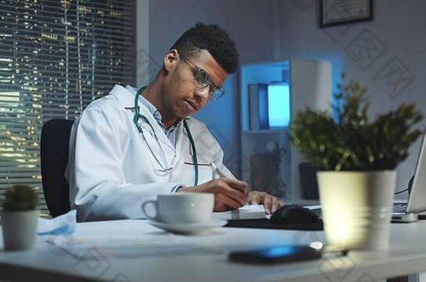 混血医生在电脑上做笔记和视频通话。因为2019冠状病毒疾病，他在家工作。
