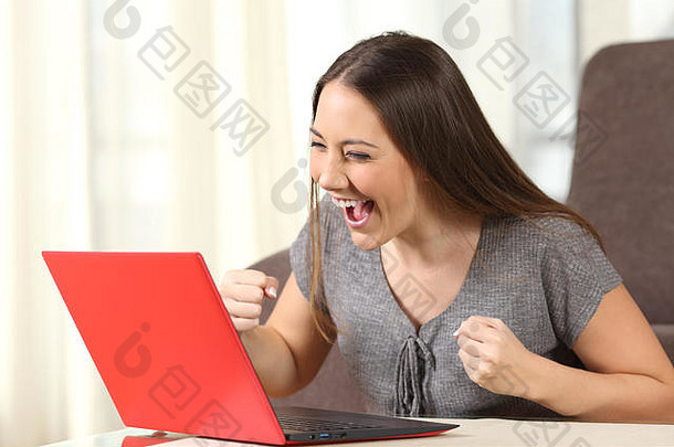 一位兴奋的女士在家里的一台红色笔记本电脑里在线阅读好消息
