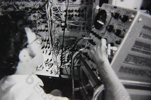 精美的70年代复古黑白生活摄影，一位专业人士在一台大型电脑的控制面板上工作。