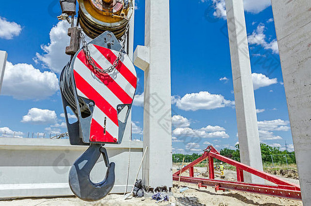 红色条纹的大吊车吊钩悬挂着，建筑工地在背景中。