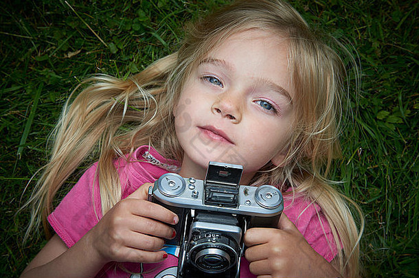 小女孩躺在草地上，用老式复古胶卷相机拍照的肖像