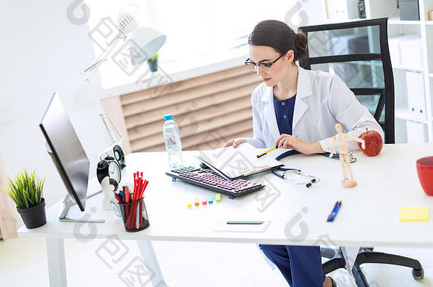 一个穿着白色长袍的漂亮女孩坐在电脑桌旁，手里拿着文件和钢笔。
