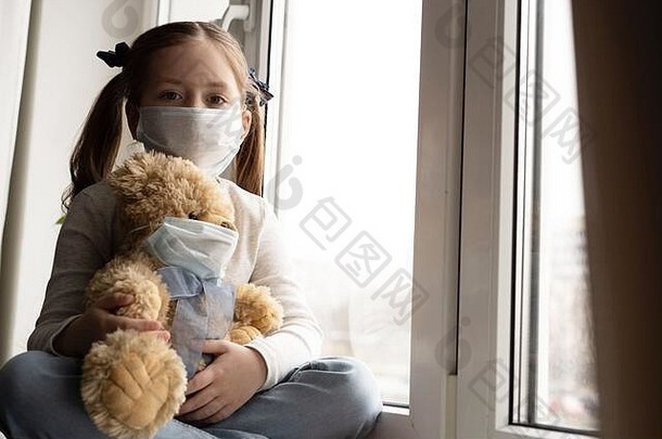 悲伤的孩子和他的泰迪熊都戴着防护面具。儿童与疾病新冠病毒-2019疾病概念