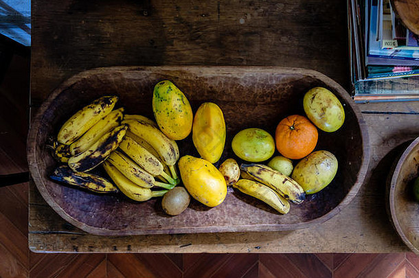 阳光照射下的木盘上的各种水果。有<strong>香蕉</strong>、桔子、木瓜