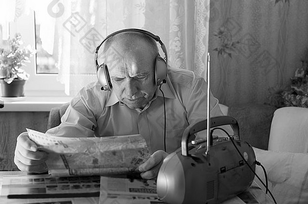 特写这位秃头老人在客厅的桌子边读<strong>小报</strong>，边用耳机听收音机里的音乐。以单色<strong>风</strong>格拍摄。。