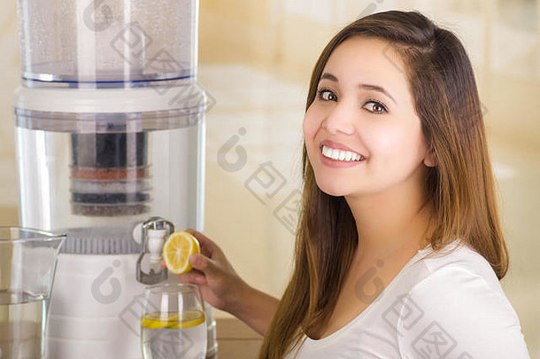 在厨房<strong>背景</strong>上，一位面带微笑的美丽女子手里拿着一个切好的柠檬，手上有一个<strong>净水器</strong>的过滤系统
