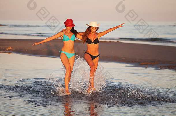 日落时分，两个穿着比基尼的漂亮女孩在海滩上散步