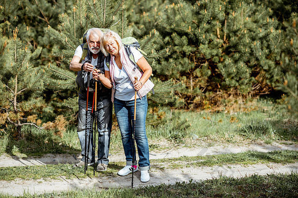 在森林里徒步旅行时，一对幸福的老年夫妇带着望远镜、背包和<strong>登山杖</strong>站在一起。退休后积极生活方式的概念
