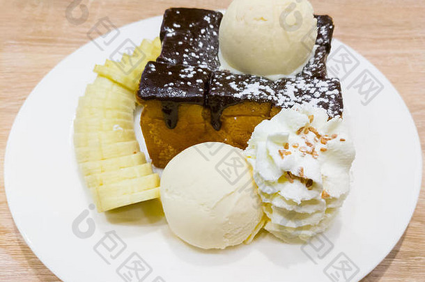 蜂蜜吐司、香草冰淇淋、鲜奶油和香蕉片放在甜点咖啡厅的木桌上。