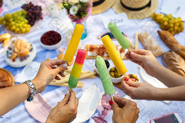 在夏日野餐的背景下，女人手拿着五颜六色的<strong>冰激凌</strong>棒。<strong>夏季</strong>周末。