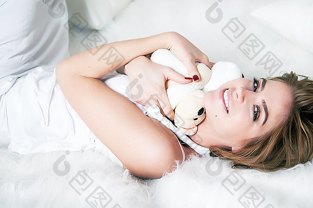 年轻的美女铺设白色床上软玩具泰迪熊圣情人节一天生日