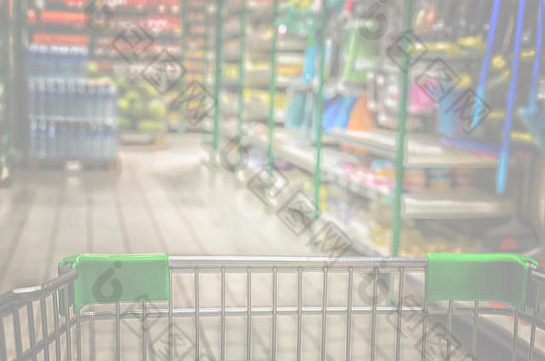 从购物车到抽象模糊超市过道背景的视图。柔和的色调