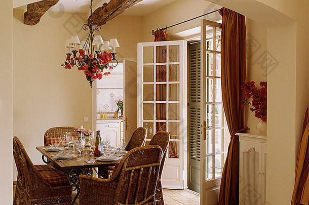 在奶油色的法国乡村餐厅，桌上放着藤椅，供午餐使用，餐厅有敞开的法式门