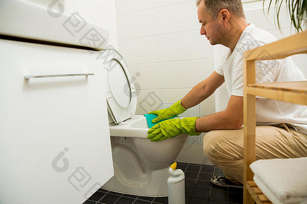 男子戴橡胶防护手套清洁，手拿刷子和清洁剂瓶清洗厕所。绿色<strong>洗衣液</strong>滴在马桶里