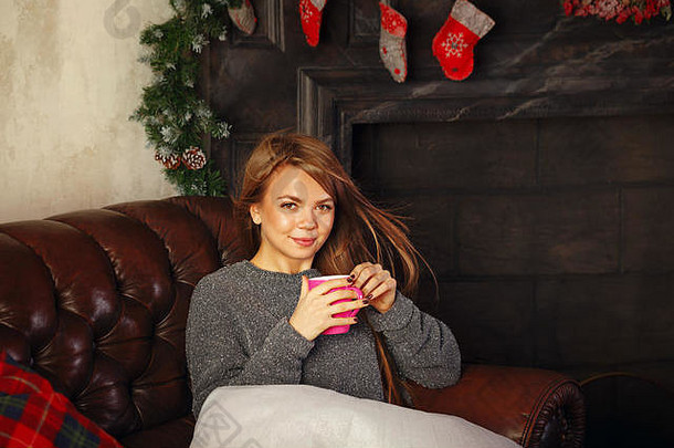 甜心迷人的女孩喝着热巧克力和棉花糖。她在沙发上。温暖的圣诞夜。