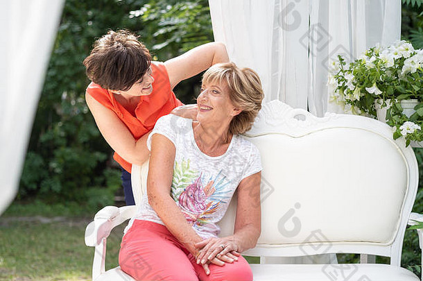 母亲和她成年的女儿微笑着拥抱着，在户外的长椅上交谈