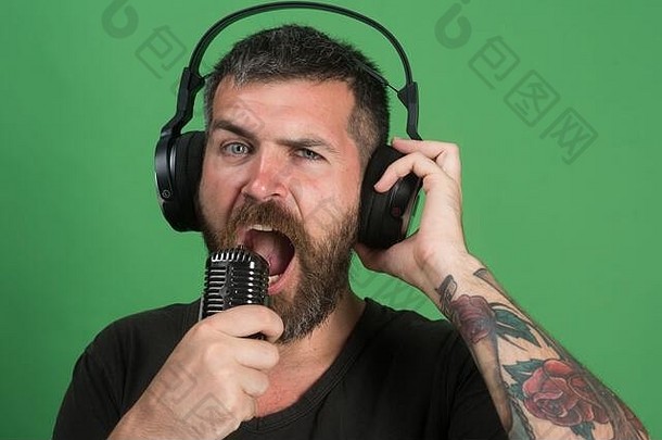 放松和音乐的概念。男人在绿色<strong>背景</strong>上<strong>唱歌</strong>，眨眼。留着胡子的Dj戴着耳机。留着胡子、脸很感兴趣的歌手喜欢音乐。