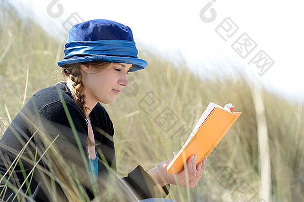 戴着蓝帽子的年轻女子在沙丘上看书