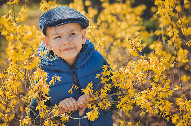 可爱英俊的男孩，穿着时髦的蓝色连衣裙，戴着黄色的帽子，享受着春天的时光。