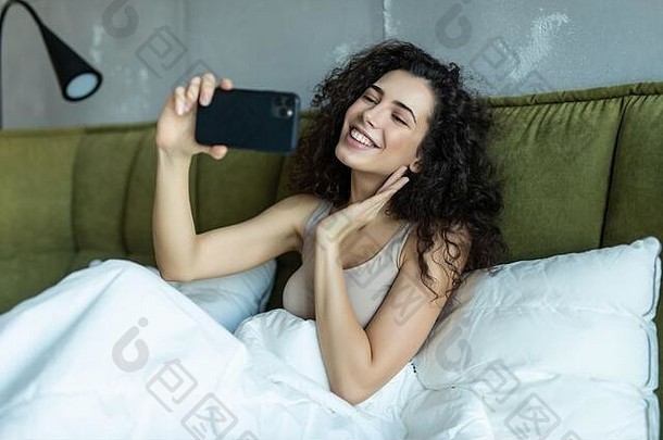 漂亮的女人采取自拍照片说谎床上白色亚麻