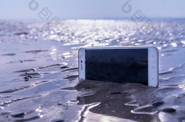 智能手机卡在沙滩上潮湿的沙子里