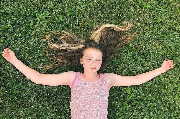 11岁女孩躺在草地上，双臂张开，脸上表情严肃