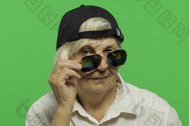 一位戴着墨镜和帽子的老妇人微笑着。穿着白衬衫的快乐老奶奶。放置您的徽标或文字。色度键。绿色屏幕背景