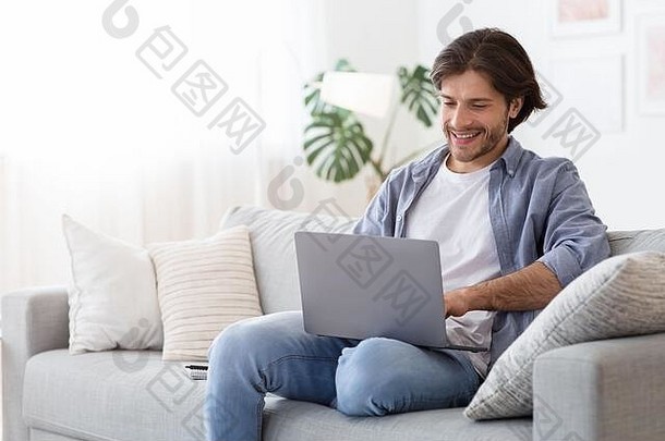 快乐男人坐在家里的沙发上用笔记本电脑打字