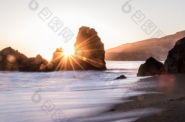 日落在金门，金色的光线将沙滩上的两块岩石与沙滩和海浪分开